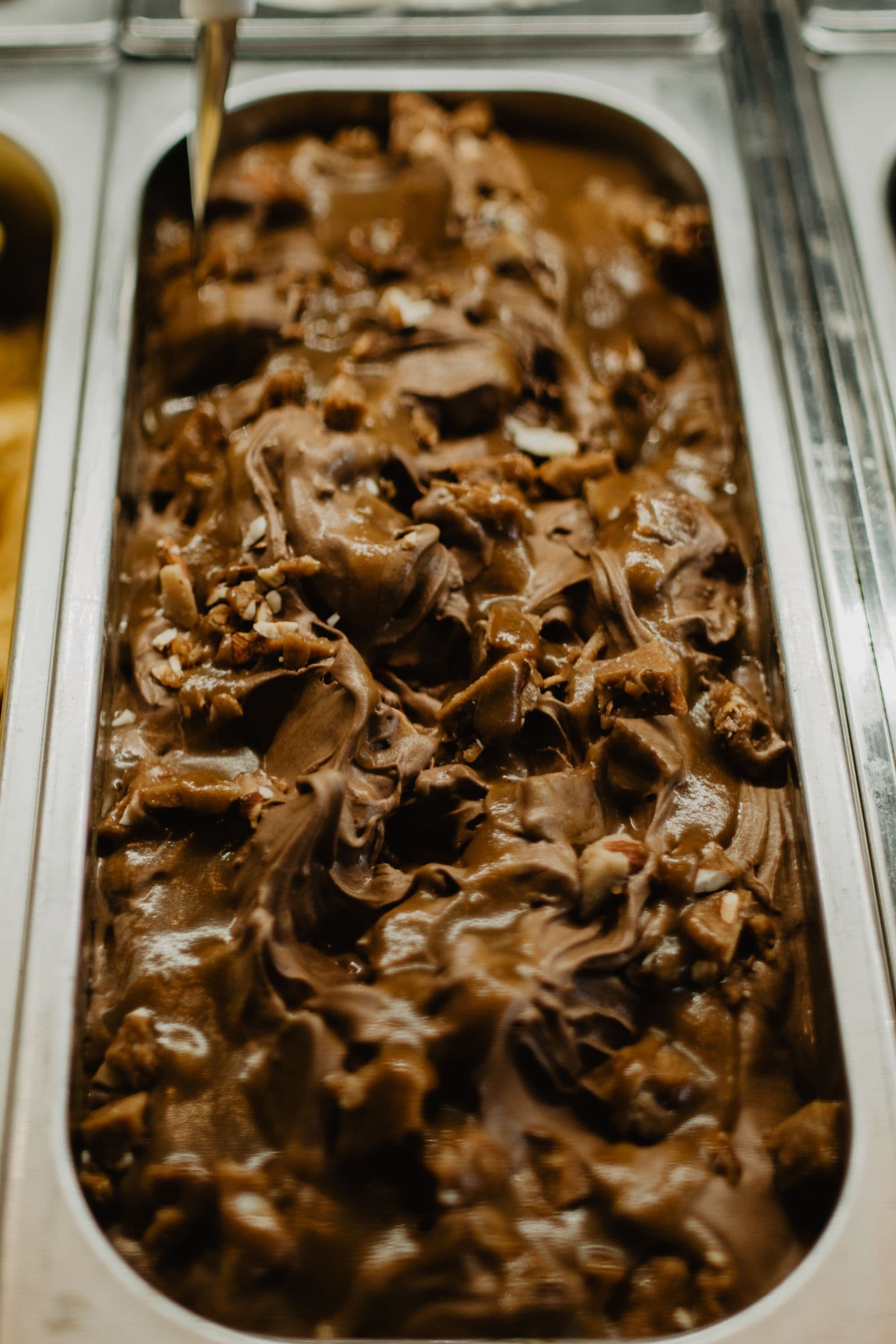A steel tray of dark chocolate gelato rippled with chocolate shards and nuts
