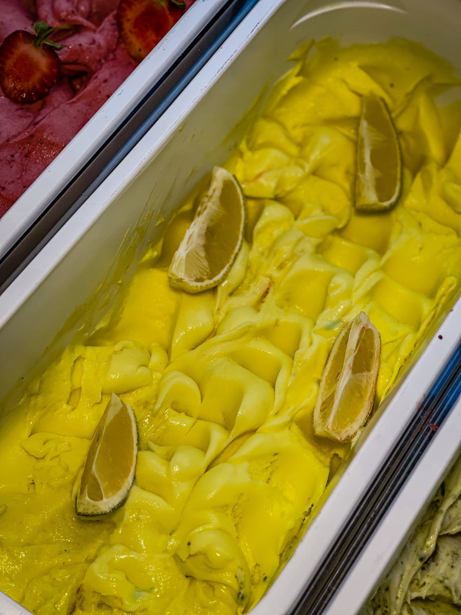 A tray of vivid yellow lemon sorbet topped with fresh lemon wedges