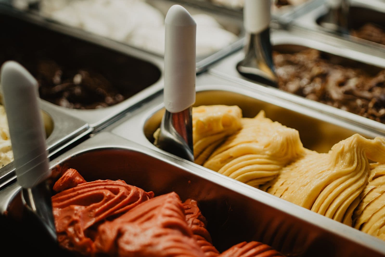 Ridged trays of red and golden gelato waiting with their spatulas