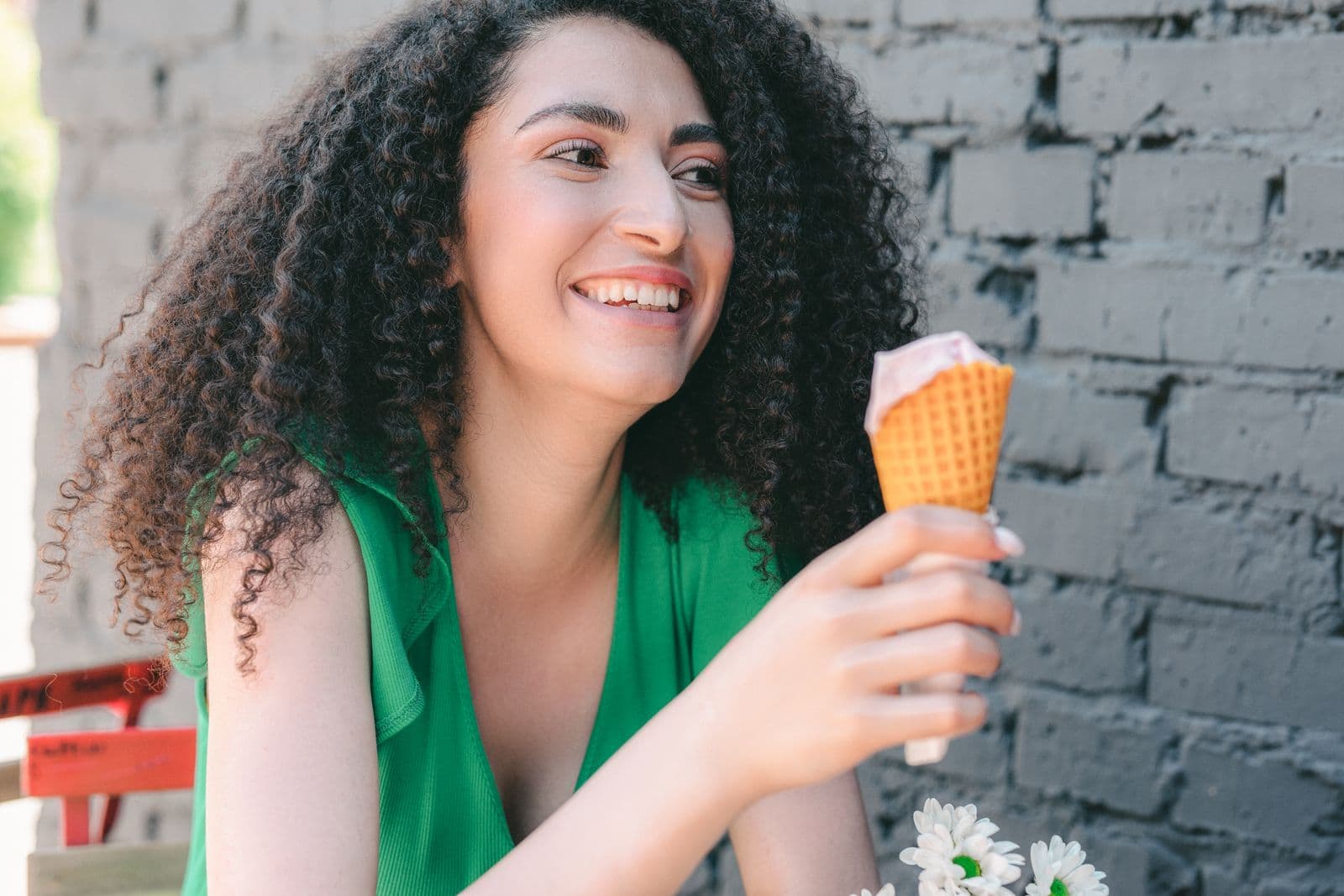 A woman in a green dress smiling with a gelato cone beside a grey brick wall