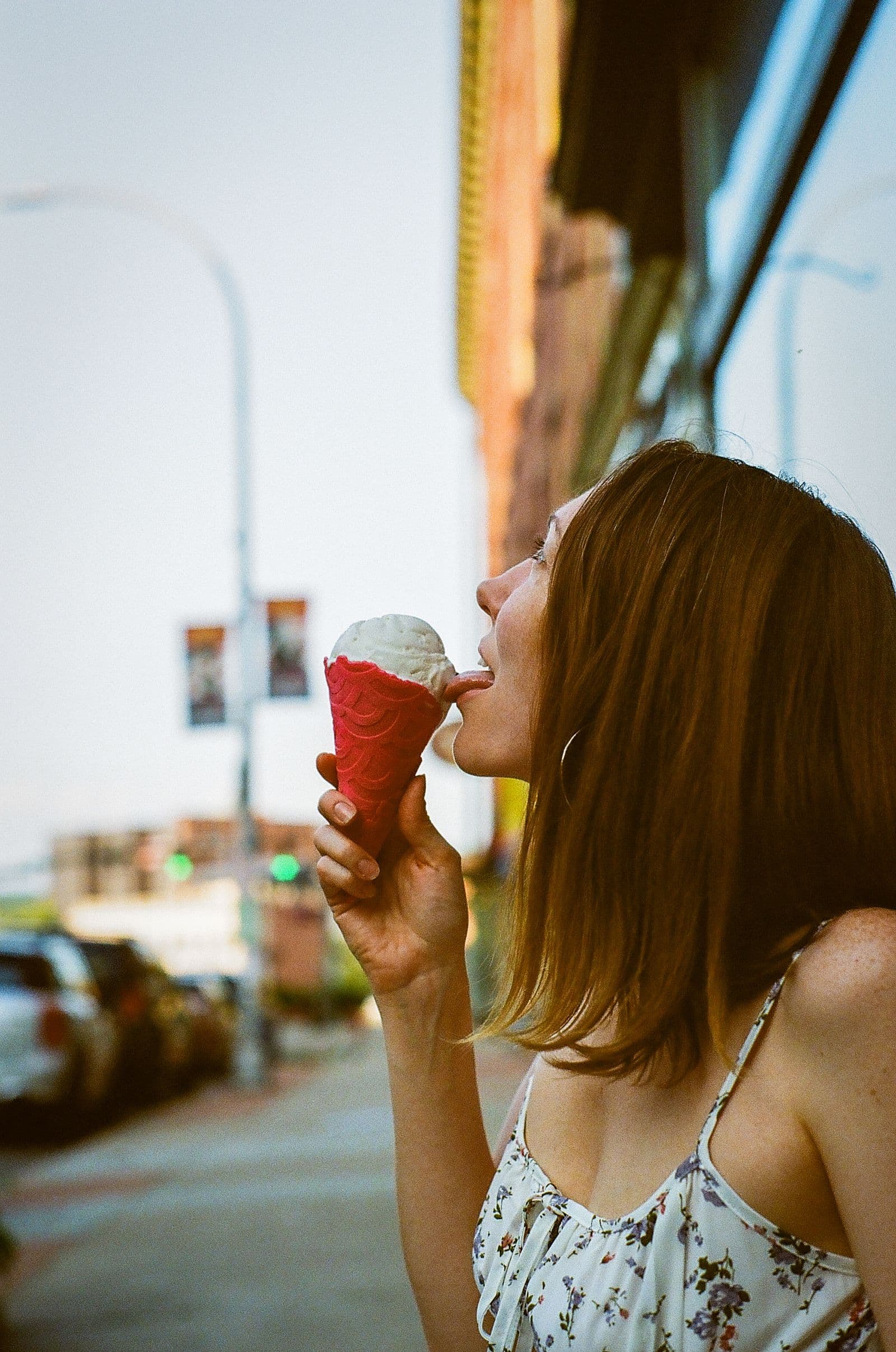 A woman on a sunlit street tasting white gelato from a bright red cone